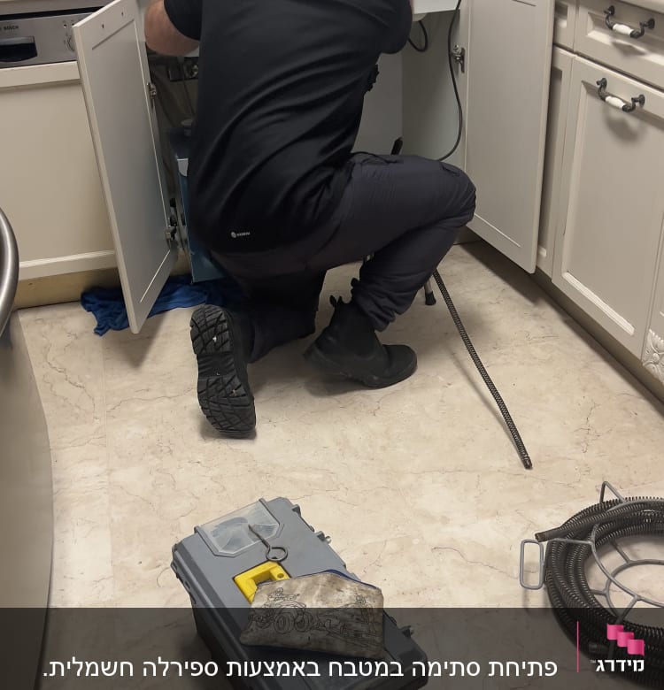 אינסטלטור עובד מתחת לכיור עם כלי עבודה וצינור